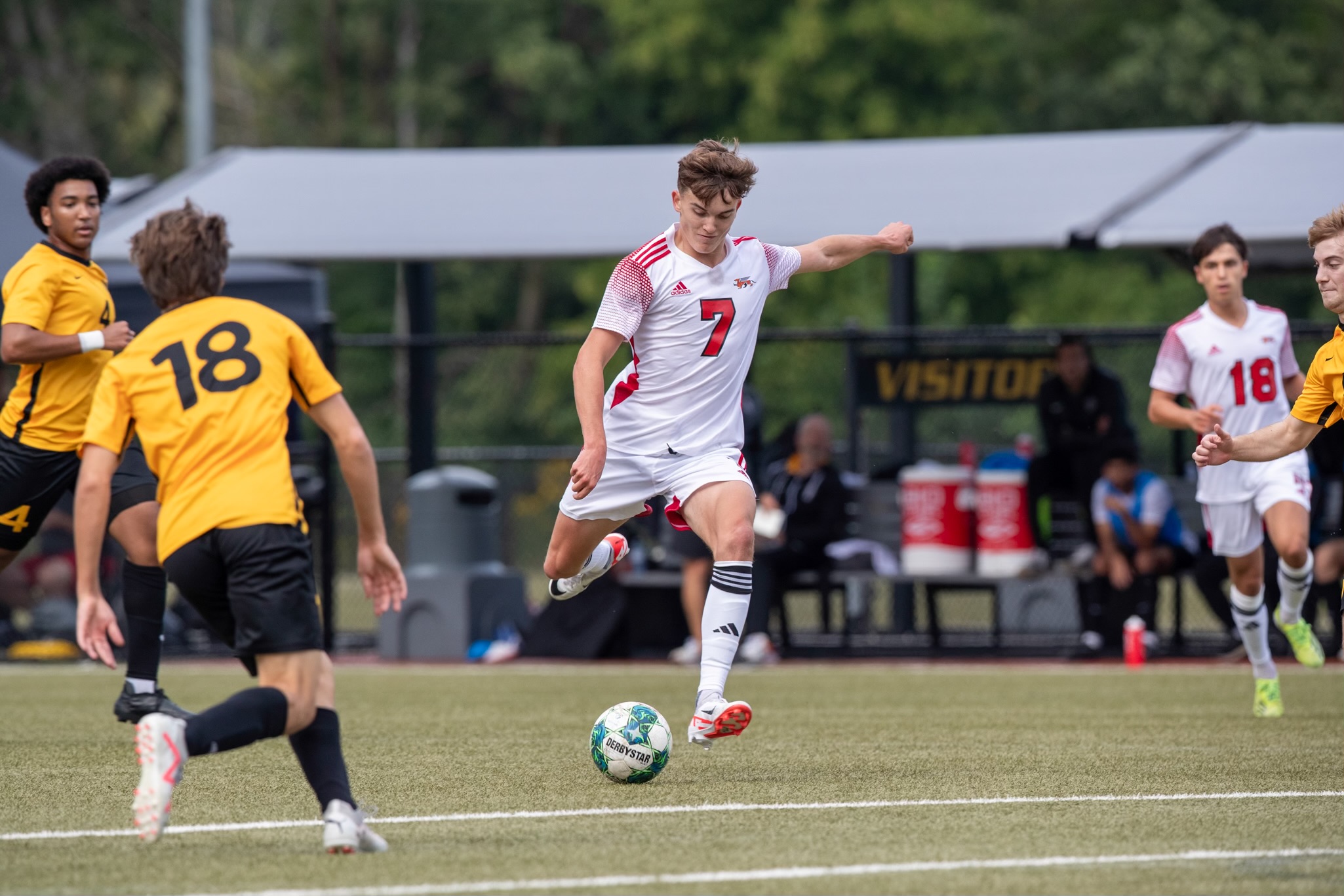 Young man in white and red soccer uniform in kicking motion on soccer field with a ball.