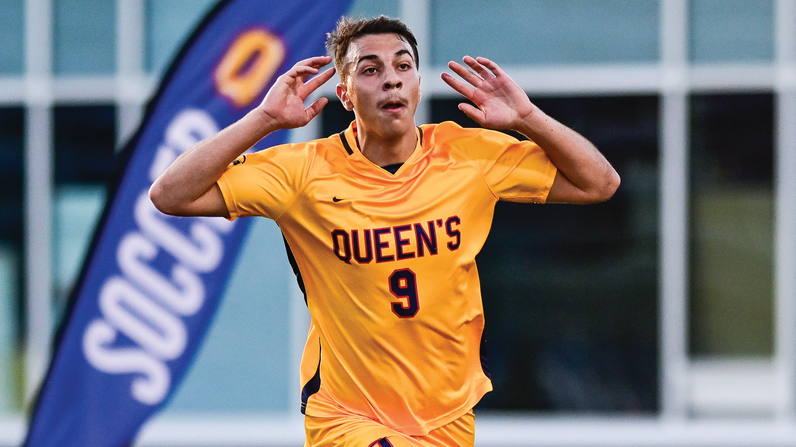 Action photo of Queen's men's soccer player Matthew Ciavarro holding his hands up to his ears encouraging crowd noise
