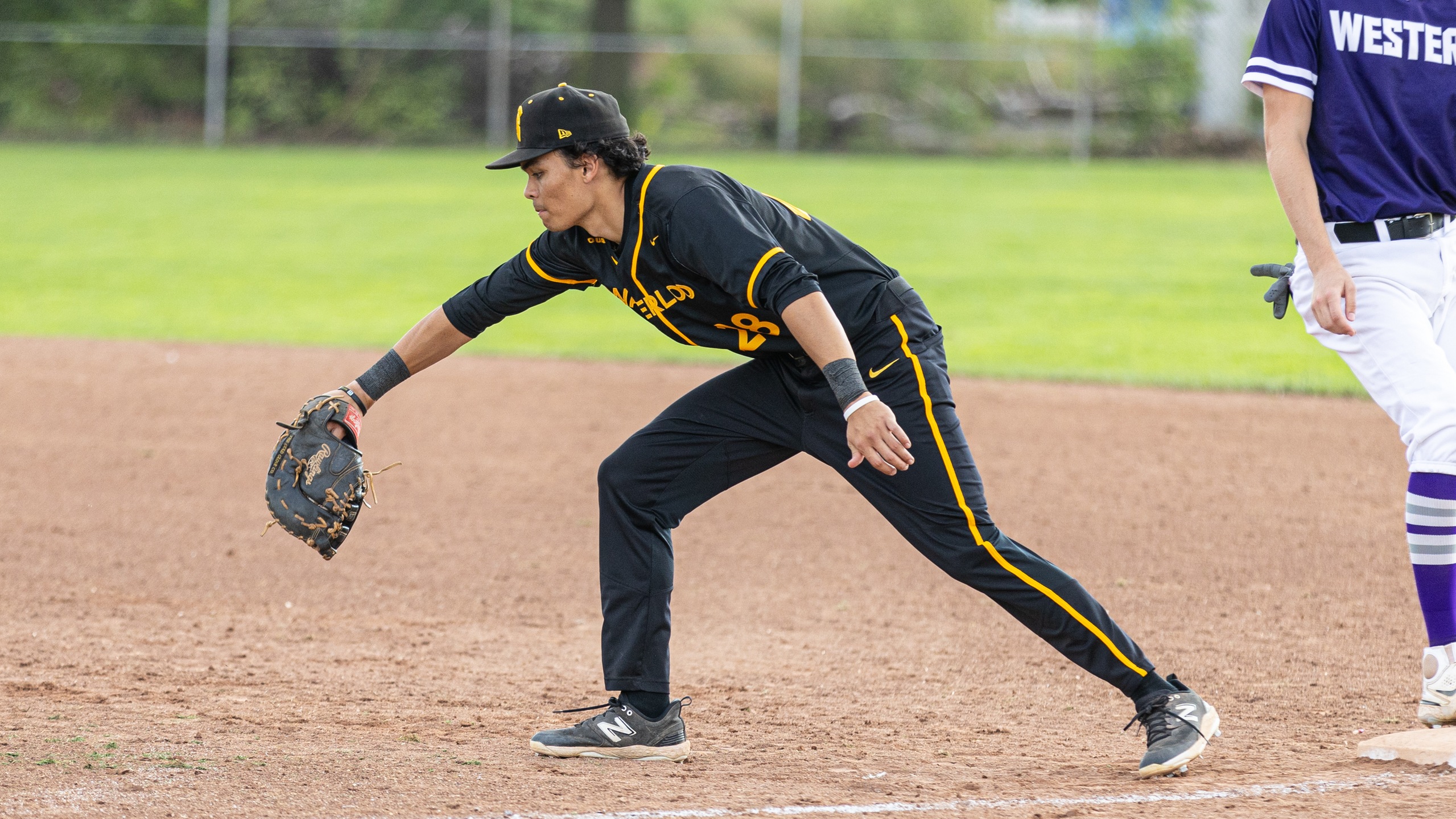 Man in baseball uniform leaning forward and reaching to catch a ball on a baseball pitch.