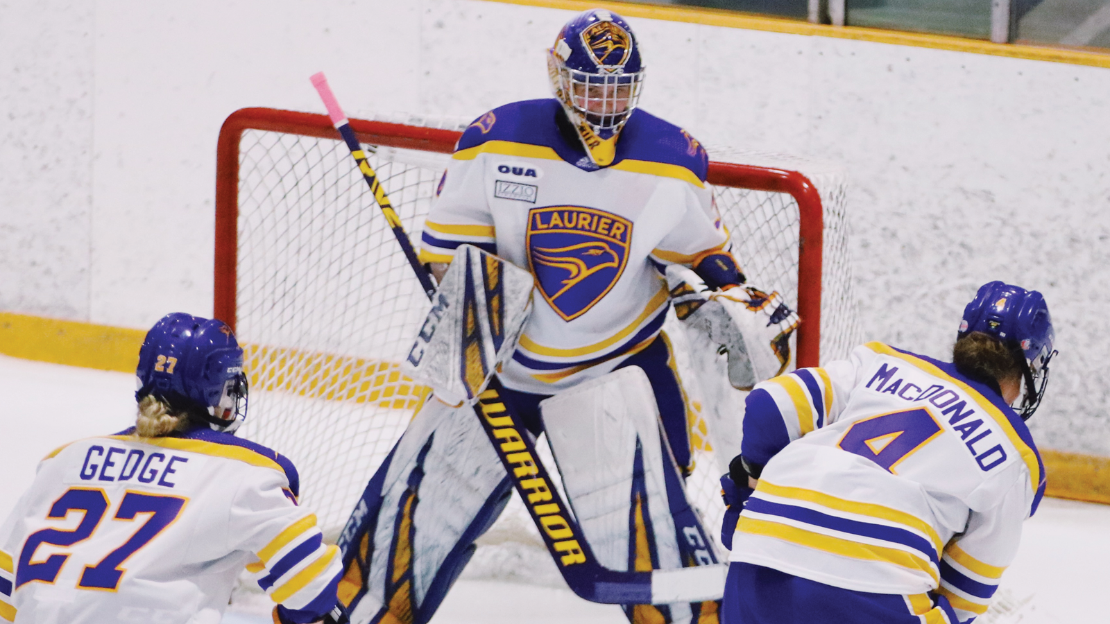 Laurier women's hockey goalie Acadia Carlson standing in her crease with a pair of teammates skating in front of her