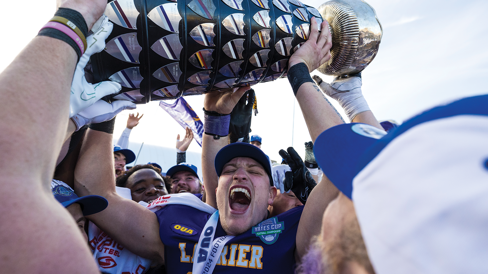 Action photo of Laurier quarterback Taylor Elgersma lifting the Yates Cup and celebrating with his team 