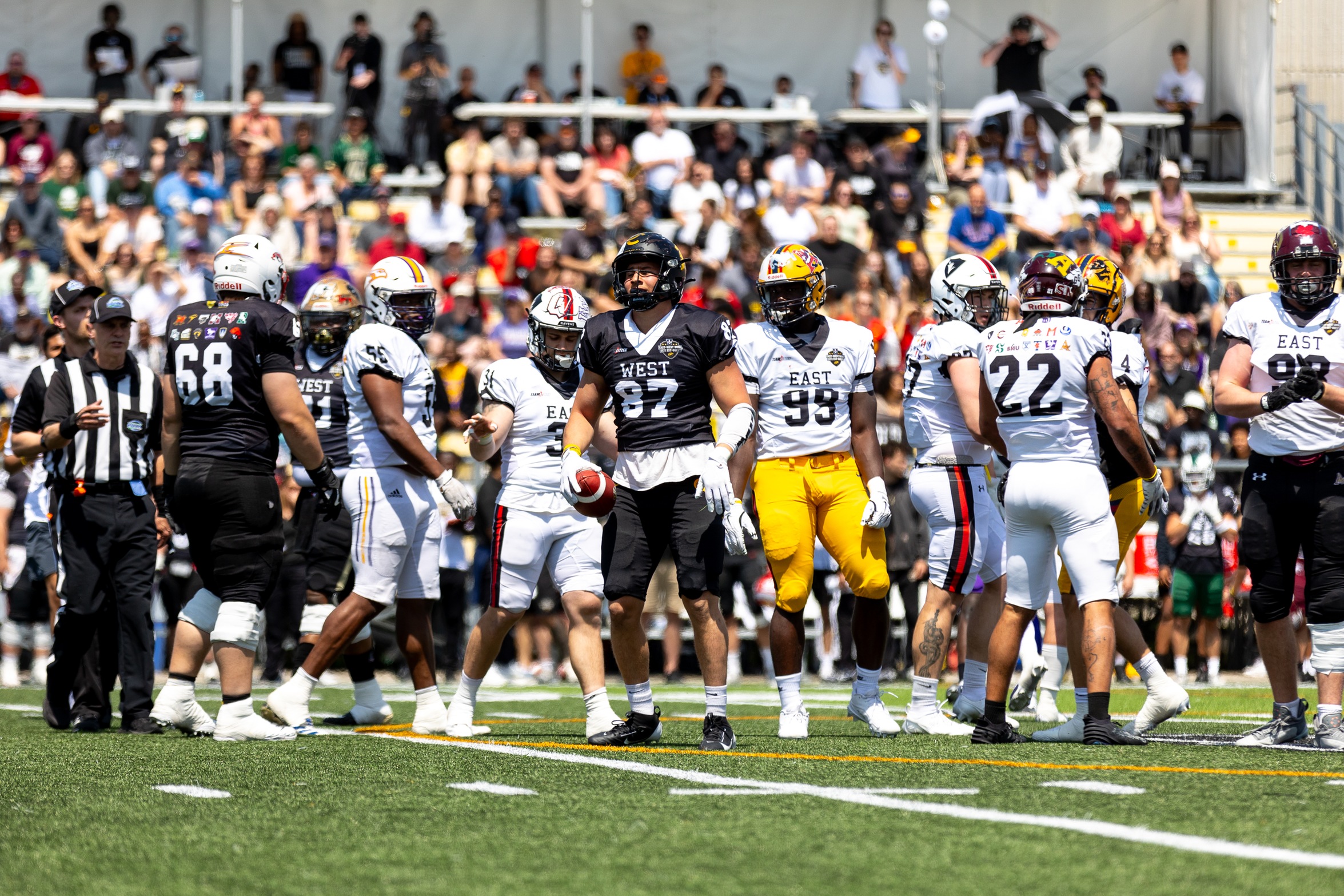 Photo of many football players after a play at the 2025 U SPORTS East West bowl in Waterloo with the crowd in the background 