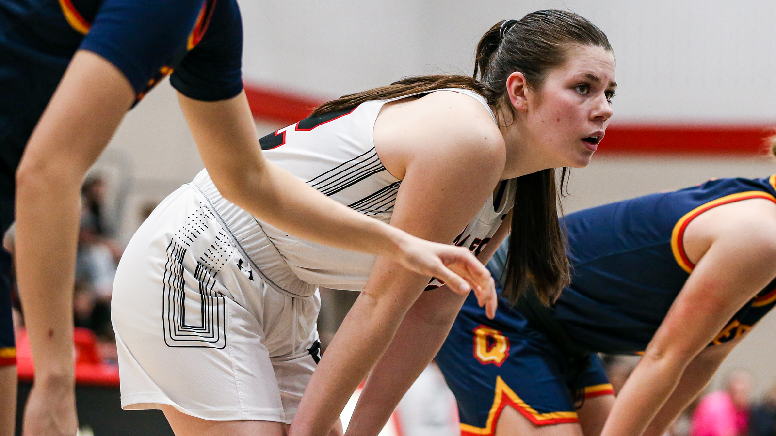 Carleton women's basketball player with her hands on her knees during a free throw attempt, between two Queen's players